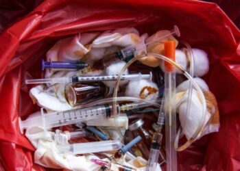 The contents of a bright red hazardous medical waste bag reveal used syringes, bandages, tubes, and ampoules.