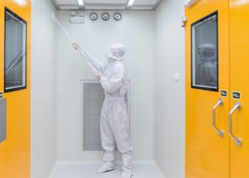 An individual wearing a white sterile gown and gloves is using a cleaning tool to scrub a white wall.