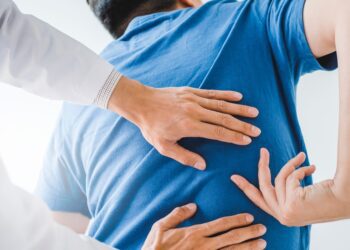A man wearing a blue shirt in a clinic pointing to where he’s feeling back pain as a chiropractor makes adjustments.