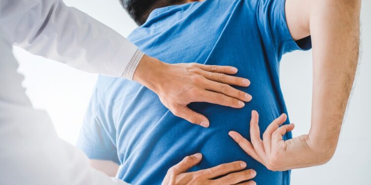A man wearing a blue shirt in a clinic pointing to where he’s feeling back pain as a chiropractor makes adjustments.
