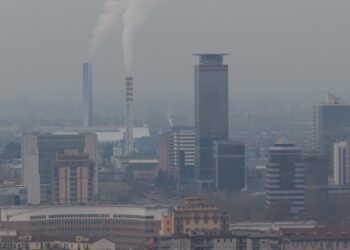 A cityscape with polluted air filling the sky. There's tall skinny smoke stacks with thick smoke releasing from the top.