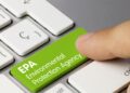A person hits a bright green button on a computer keyboard that reads 'EPA Environmental Protection Agency'