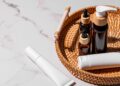 Amber glass bottles, white cream tubes, and skincare products are for daily use on a rattan tray with a marble background.