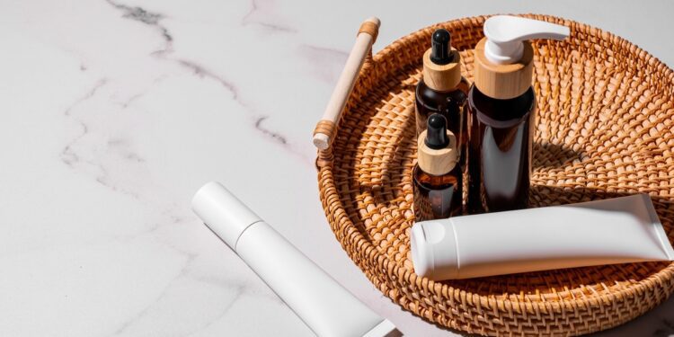 Amber glass bottles, white cream tubes, and skincare products are for daily use on a rattan tray with a marble background.