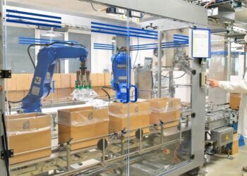 A person wearing a white hair net, a white coat, and white pants presses a button on a large packaging machine.