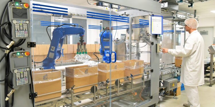 A person wearing a white hair net, a white coat, and white pants presses a button on a large packaging machine.