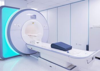 A high-tech MRI machine sits in a room at a hospital. A decorative panel on the side of the machine glows blue.