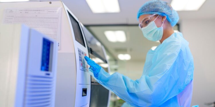 A healthcare professional wearing a mask, hair net, gloves, and clean room suit, working an a large medical device.