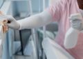 A hospital employee cleans surfaces in a patient's recovery room with a bottle of cleaning solution and a rag.