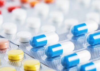 An extreme close-up of individually-sealed pills. The pills are a combination of yellow, red, white, and blue.