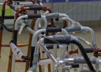 A group of canes, crutches, and other mobility devices stacked in a row together. They are all in an empty room.