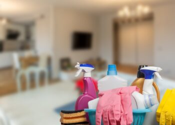 A close-up of a selection of cleaning supplies on a table with a blurry background of a home gathering space.