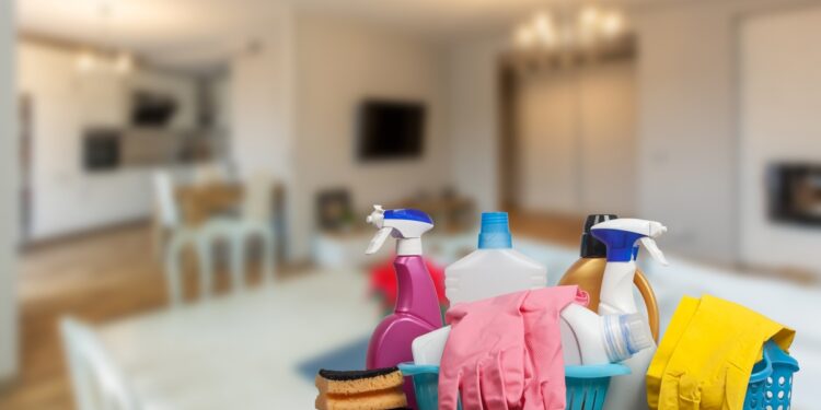 A close-up of a selection of cleaning supplies on a table with a blurry background of a home gathering space.