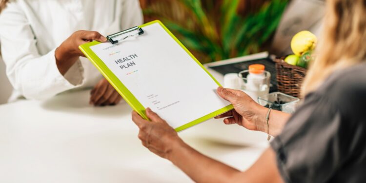 A functional medicine provider handing a clipboard to a patient. The clipboard has a document on it that reads “Health Plan”.