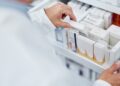 A pharmacist opening a drawer filled with assorted boxes of medicine and grabbing one of them from the middle.