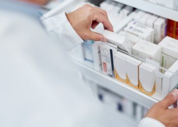 A pharmacist opening a drawer filled with assorted boxes of medicine and grabbing one of them from the middle.