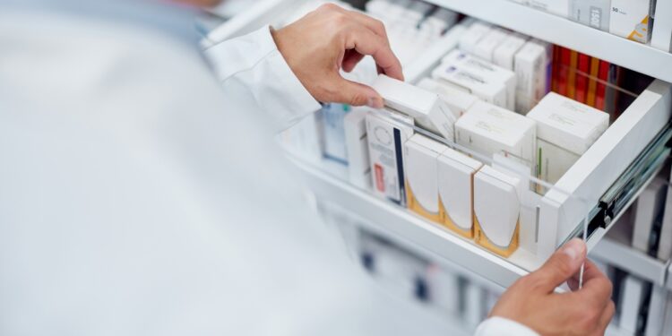 A pharmacist opening a drawer filled with assorted boxes of medicine and grabbing one of them from the middle.