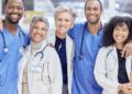 A team of healthcare professionals wearing scrubs and lab coats stands together and smiles in a bright clinic.