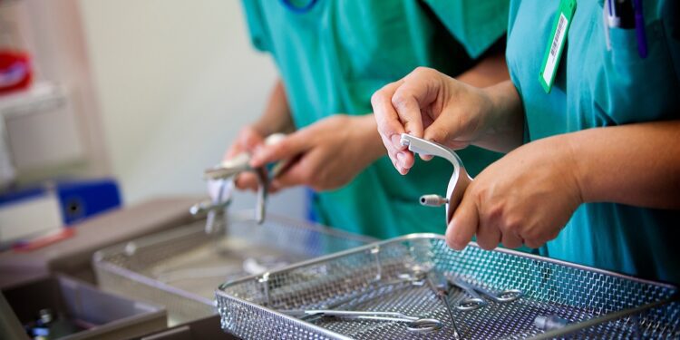 Healthcare professionals in scrubs inspect surgical instruments over a metal sterilization basket in a clinical setting.