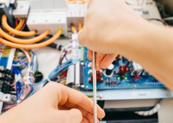 A technician is using a screwdriver to repair a laboratory equipment electronic device with exposed wiring.