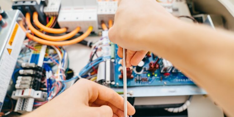 A technician is using a screwdriver to repair a laboratory equipment electronic device with exposed wiring.
