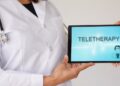 A close-up of a woman in a doctor's coat with a stethoscope holding an electronic tablet that says "TELETHERAPY."
