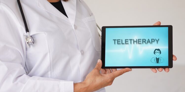 A close-up of a woman in a doctor's coat with a stethoscope holding an electronic tablet that says "TELETHERAPY."