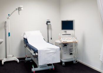 A room with black floors, a white curtain hanging from the ceiling bundled to the side, and a medical bed.