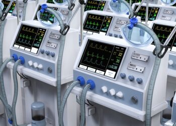 Rows of medical ventilators with breathing tubes and digital monitoring screens displaying patient vital signs.