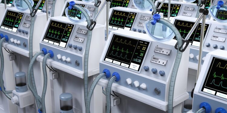 Rows of medical ventilators with breathing tubes and digital monitoring screens displaying patient vital signs.